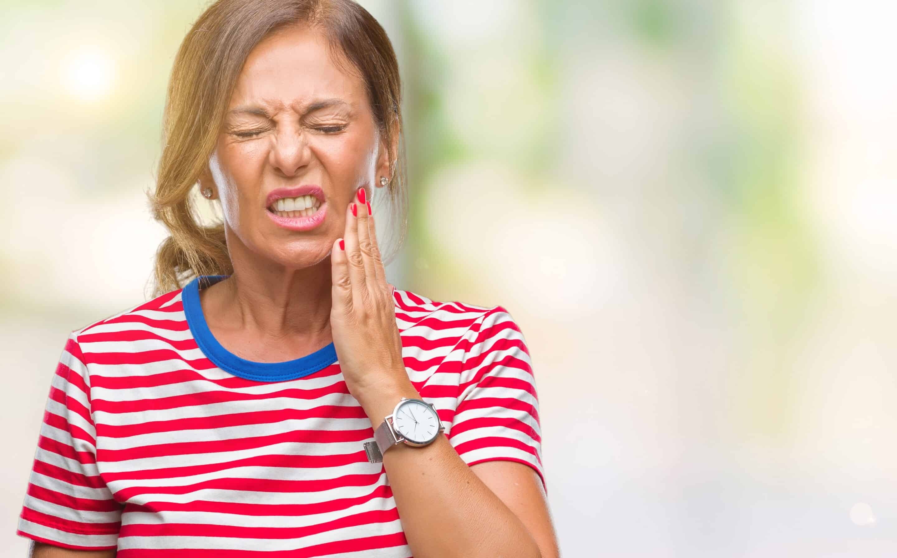 Emergency Dentistry in Chandler Woman experiencing tooth pain, holding her cheek in discomfort while wearing red striped shirt.